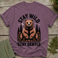 T-shirt with a graphic of a bear, trees, and moon with text "STAY WILD STAY GENTLE".