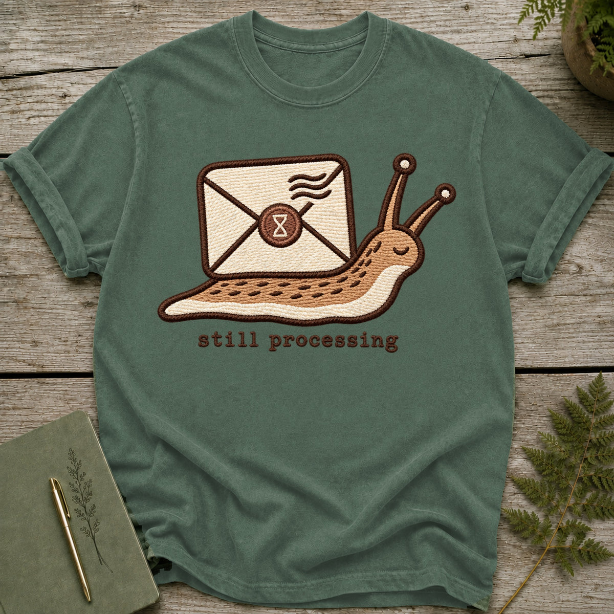 Green t-shirt with embroidered slug carrying an envelope and the text "still processing".