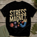 Black t-shirt with "STRESS MAGNET" text and a magnet attracting yarn balls.