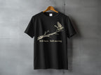 Black t-shirt with a bird on a branch and text "Still here Still moving."