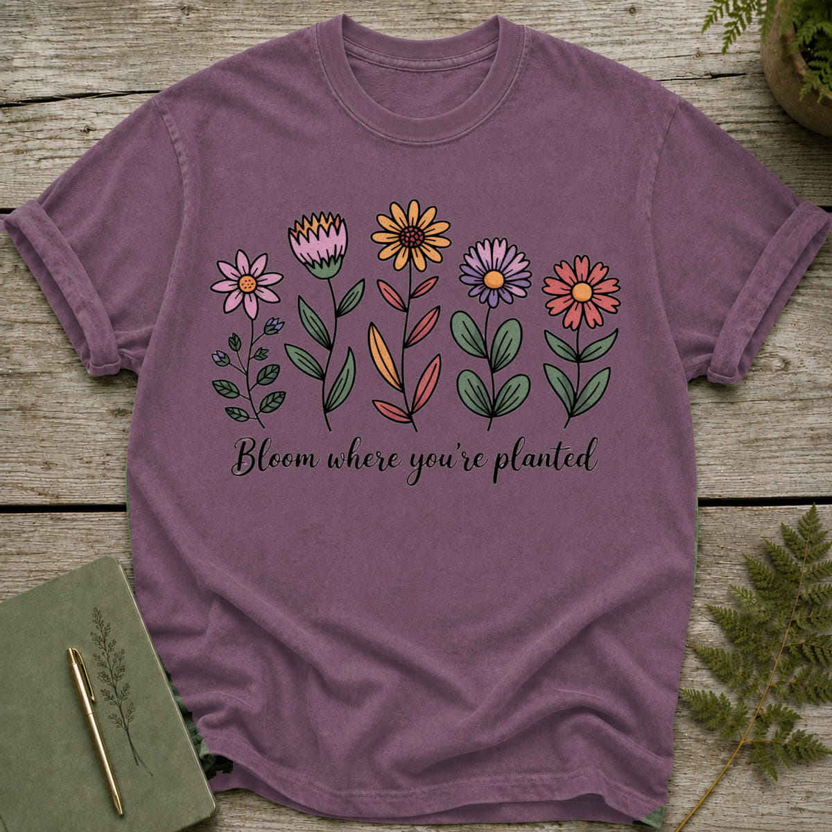 Purple t-shirt with colorful floral illustration and "Bloom where you're planted" text.
