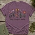 Purple t-shirt with colorful floral illustration and "Bloom where you're planted" text.