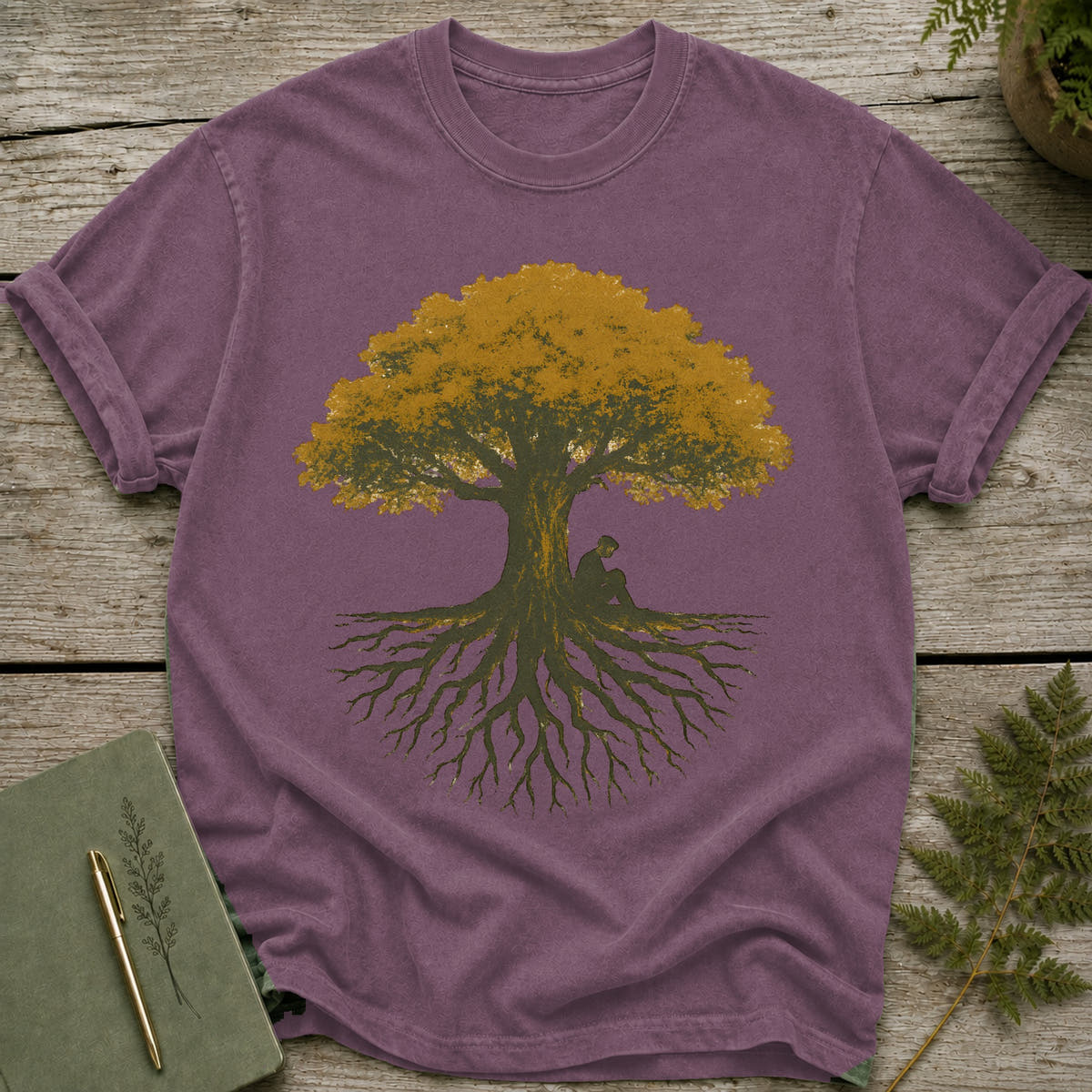 Purple t-shirt with a graphic of a person sitting under a large tree with extensive roots.