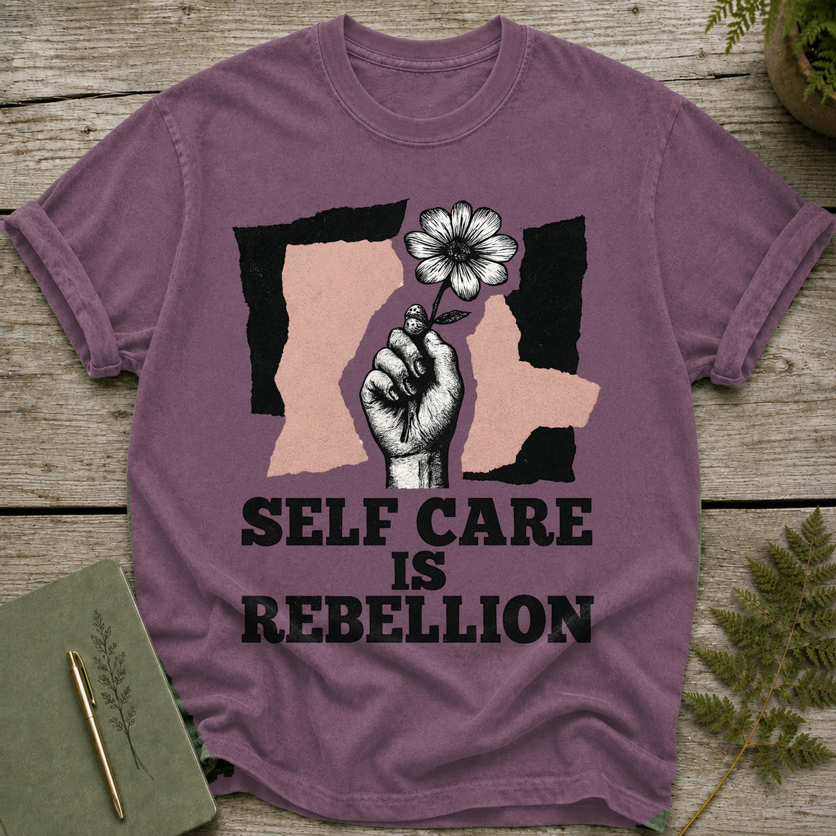 Purple t-shirt with graphic of hand holding flower and text "SELF CARE IS REBELLION".