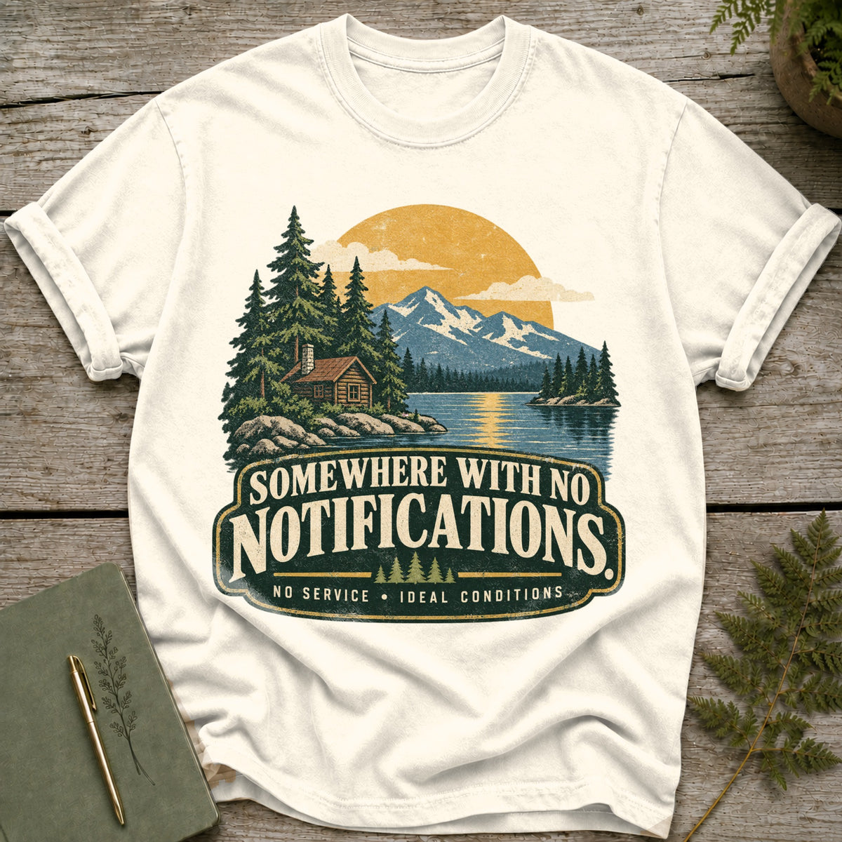 T-shirt with a graphic of a cabin by a lake, mountains, and the text "Somewhere With No Notifications".