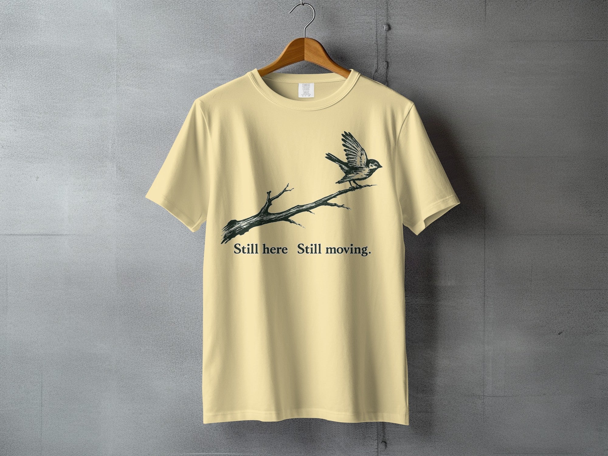 Light yellow t-shirt with a bird on a branch graphic and text.