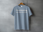 Light blue t-shirt with "Overthinking but make it 🌲 scenic" text.