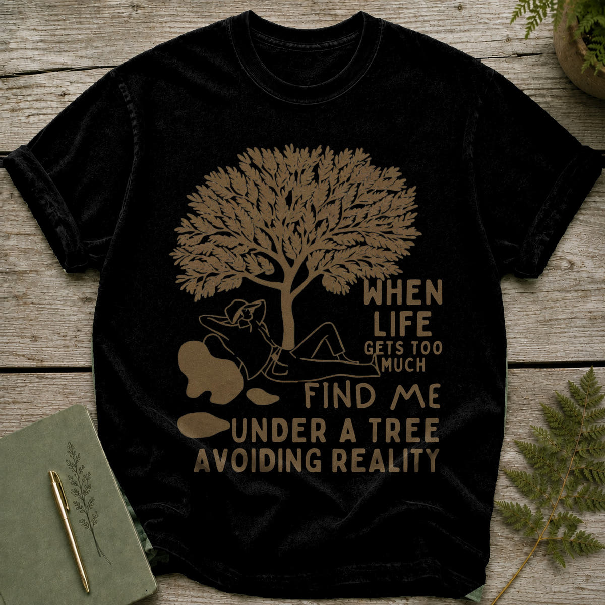 Black t-shirt with graphic of person under tree and text "When life gets too much find me under a tree avoiding reality".