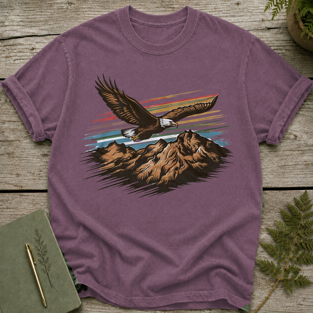 Purple t-shirt with a graphic of an eagle flying over mountains and a striped sky.