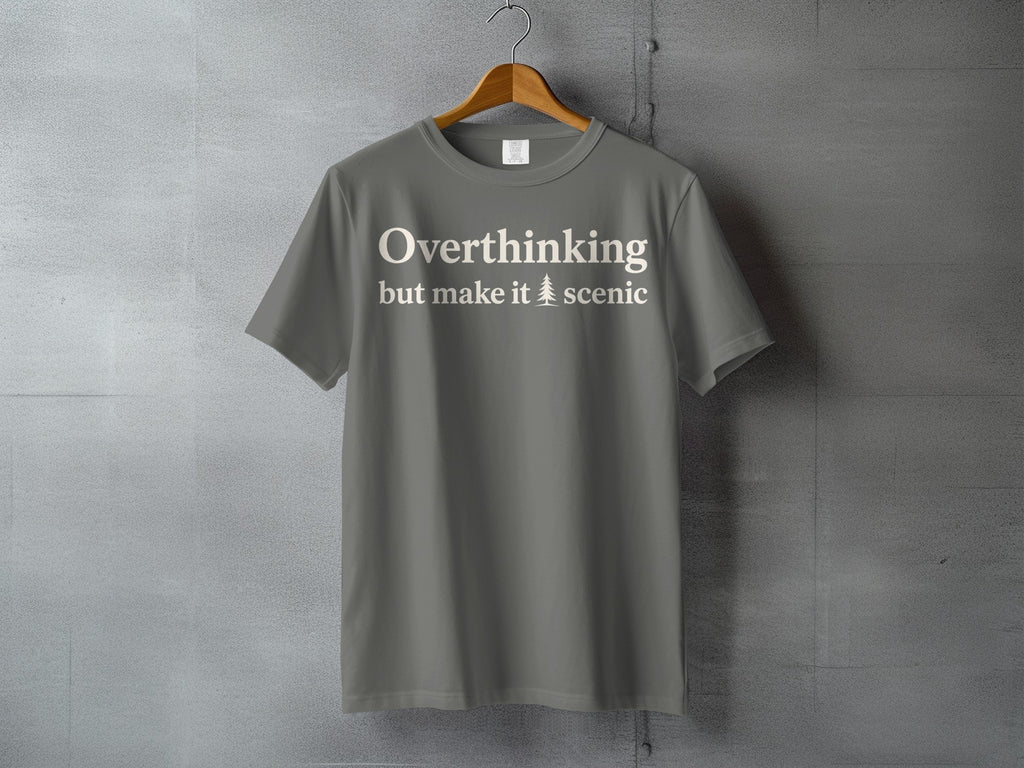 Grey t-shirt with white text "Overthinking but make it scenic" and a pine tree icon.