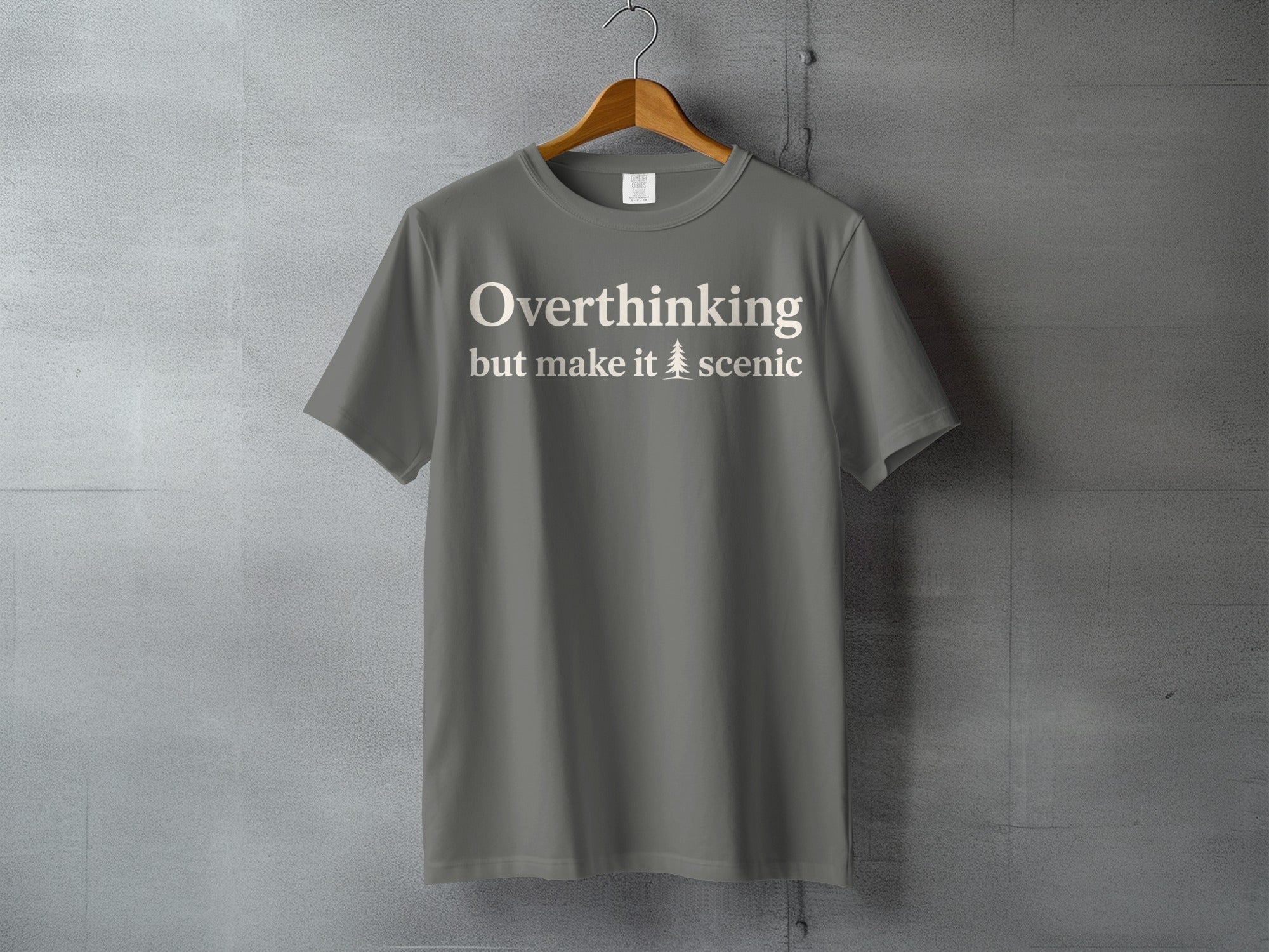 Grey t-shirt with white text "Overthinking but make it scenic" and a pine tree icon.