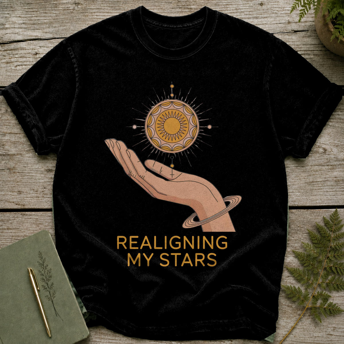 Black t-shirt with a hand holding a sun graphic and text "REALIGNING MY STARS".