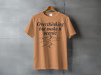 Orange t-shirt with "Overthinking but make it scenic" and mountain graphic.