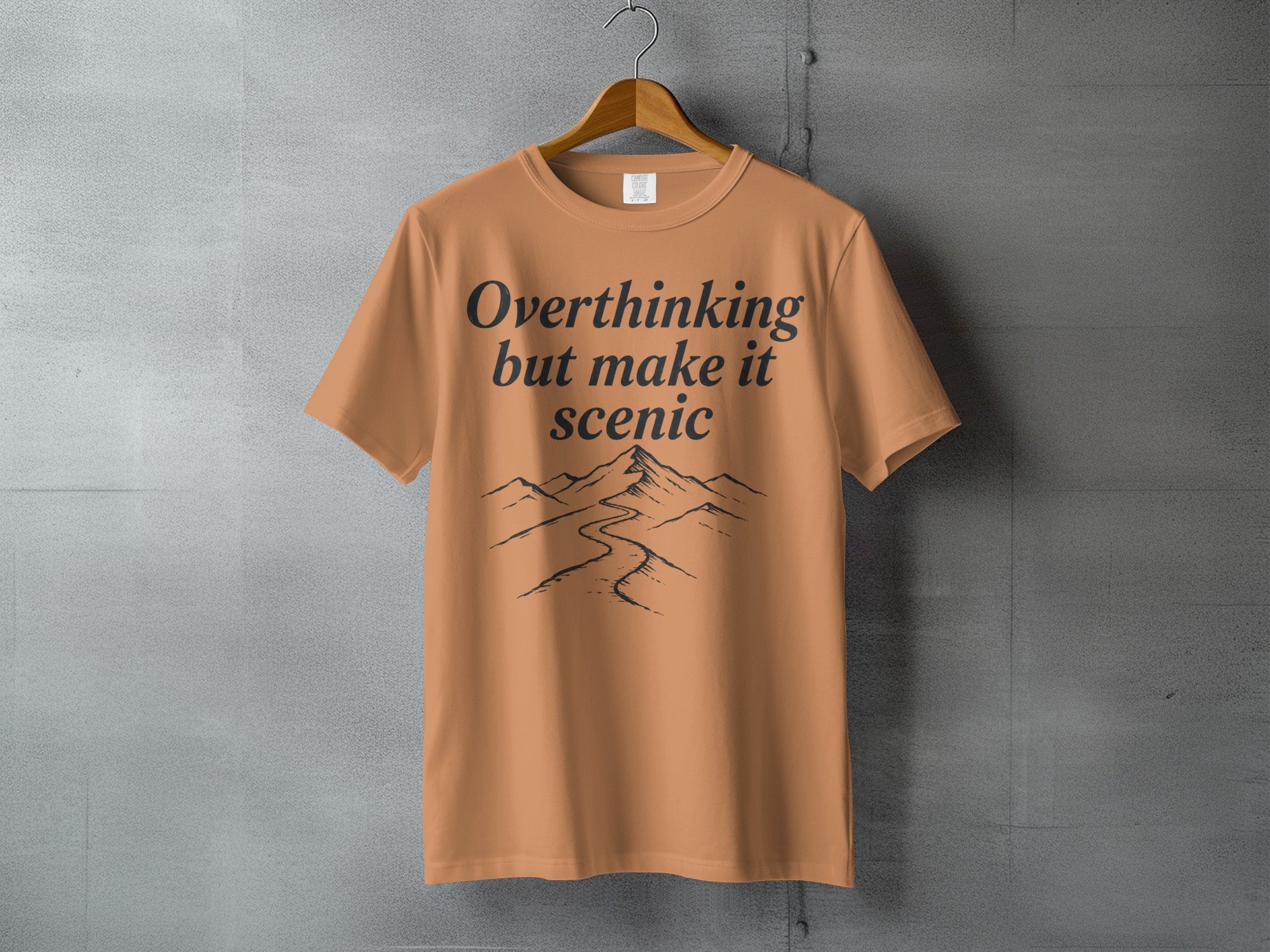 Orange t-shirt with "Overthinking but make it scenic" and mountain graphic.