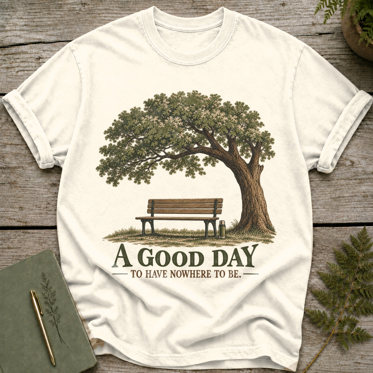 Cream t-shirt graphic featuring a tree, bench, and the text "A GOOD DAY TO HAVE NOWHERE TO BE."