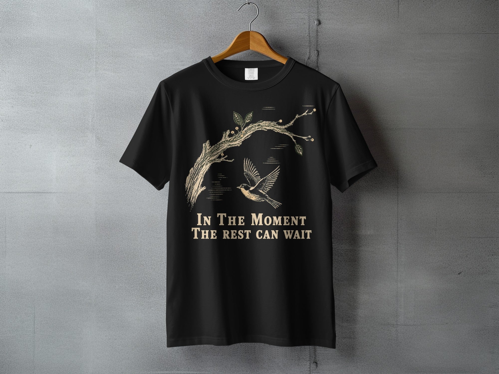 Black t-shirt with a bird and tree branch design and text "IN THE MOMENT THE REST CAN WAIT".