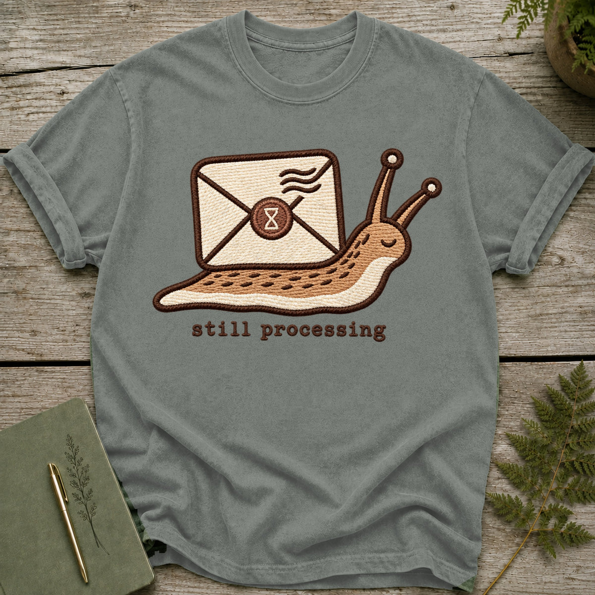 Grey t-shirt with embroidered snail carrying an envelope and the text "still processing".