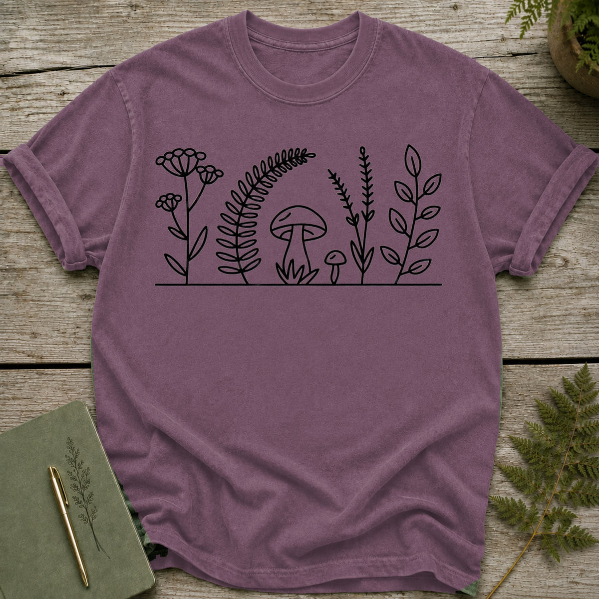Purple t-shirt with black line drawing of plants and mushrooms.