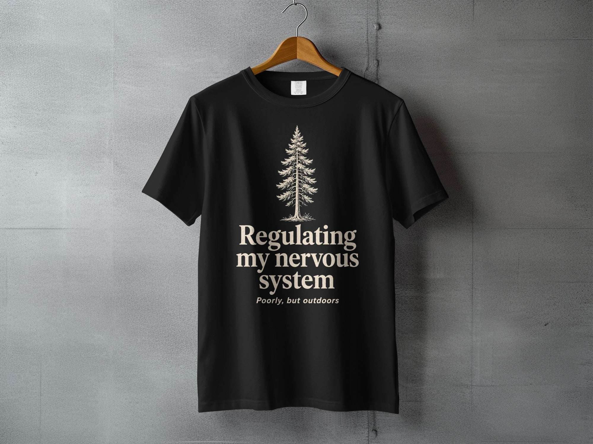 Black t-shirt with a pine tree and "Regulating my nervous system poorly, but outdoors" text.