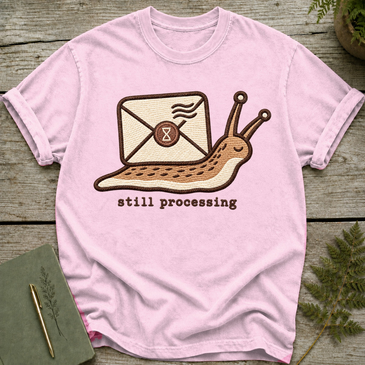Pink t-shirt with embroidered snail carrying an envelope and text "still processing".