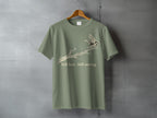 Olive green t-shirt with bird on branch graphic and text "Still here Still moving."