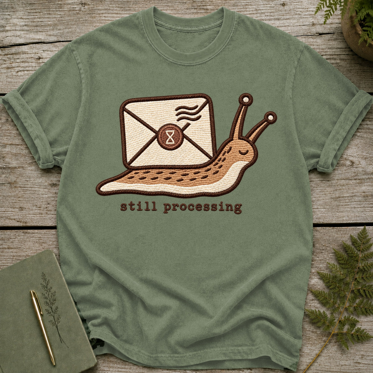 Green t-shirt with embroidered snail carrying envelope and text "still processing".