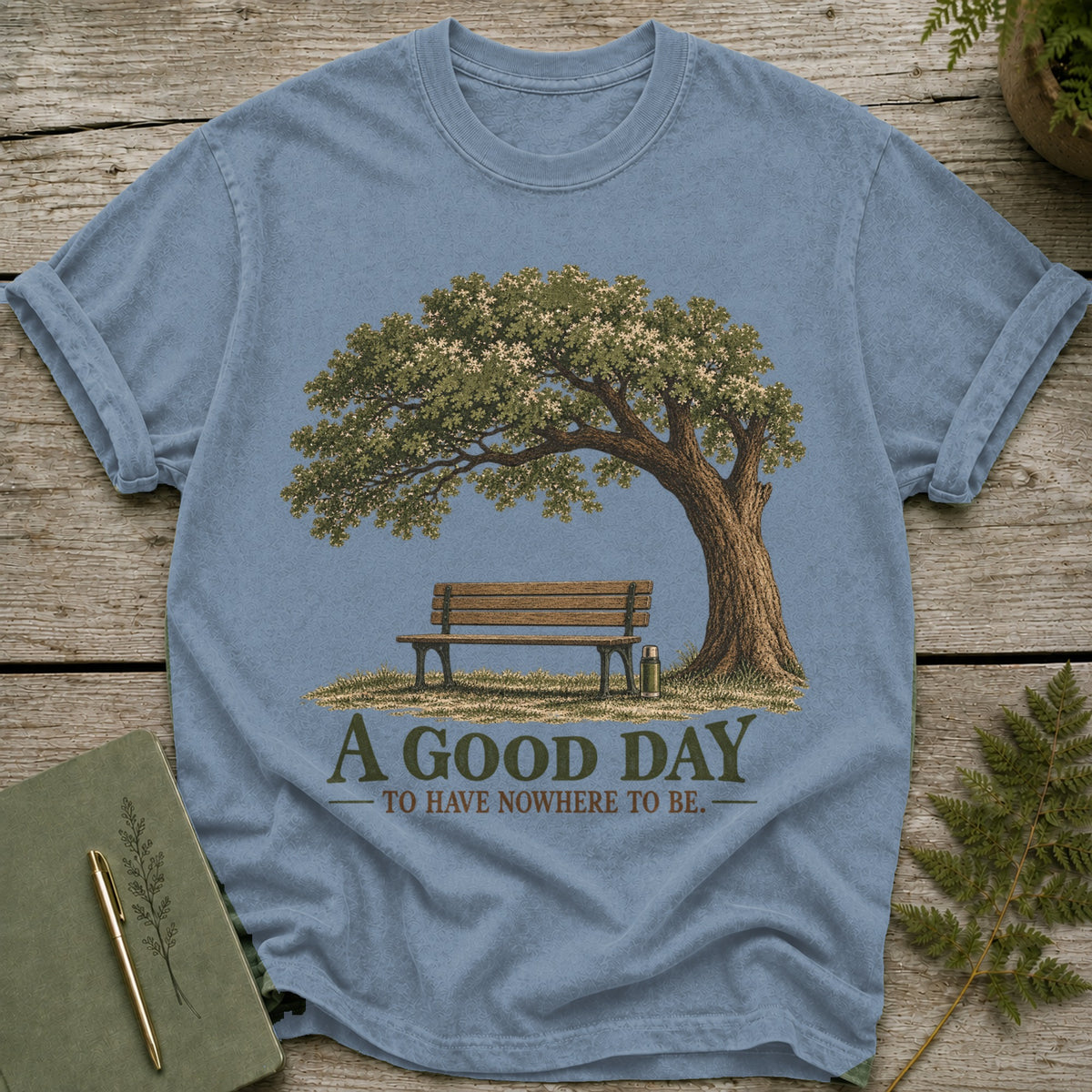 Light blue t-shirt graphic of a bench under a tree with text: A Good Day to Have Nowhere to Be.