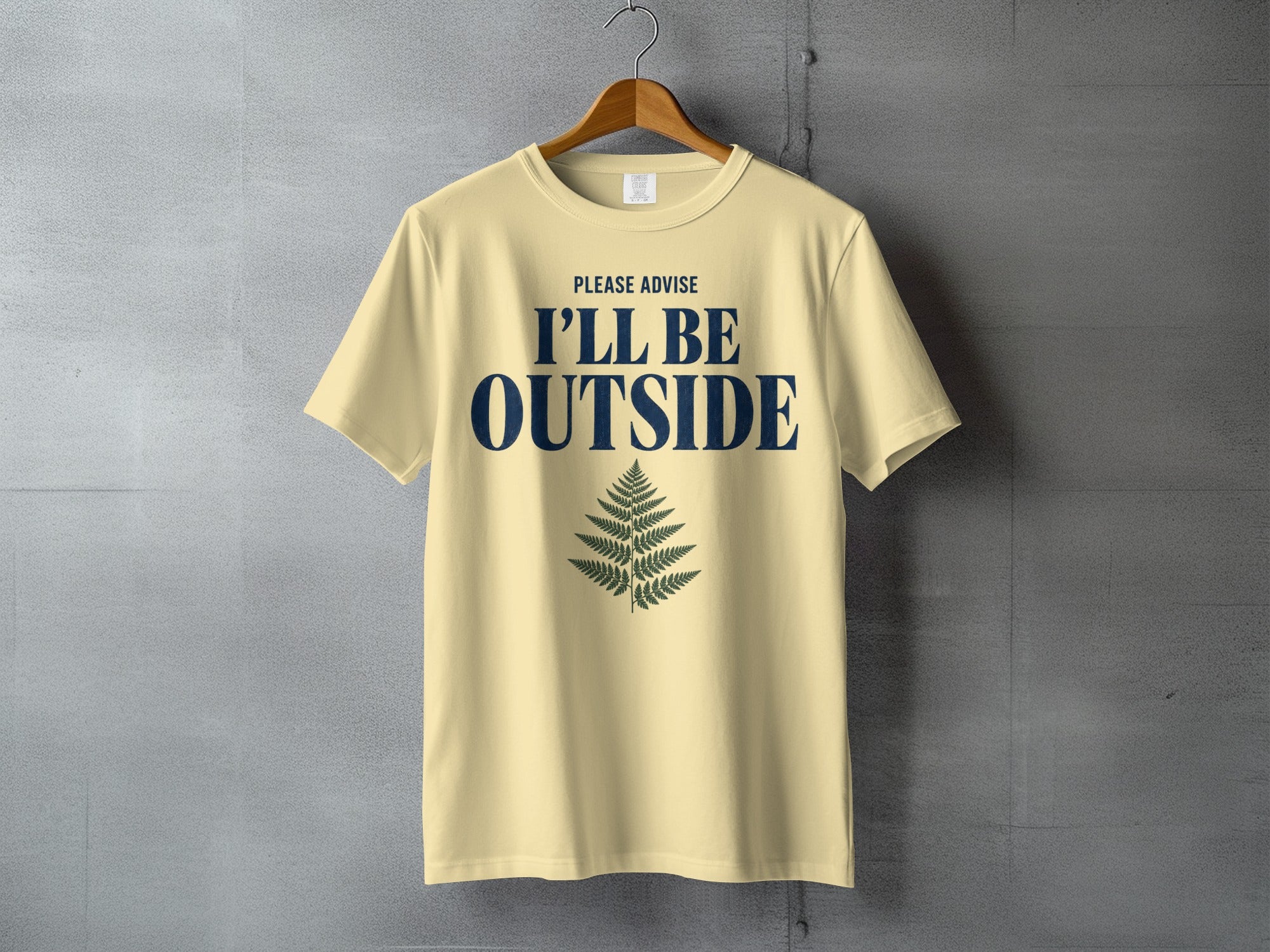 Light yellow t-shirt with navy text "PLEASE ADVISE I'LL BE OUTSIDE" and a fern graphic.