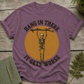 Purple t-shirt with skeleton hanging from branch, text "Hang in there it gets worse."