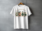 White t-shirt with four ducks reading books and the text "Softly spiraling still moving."