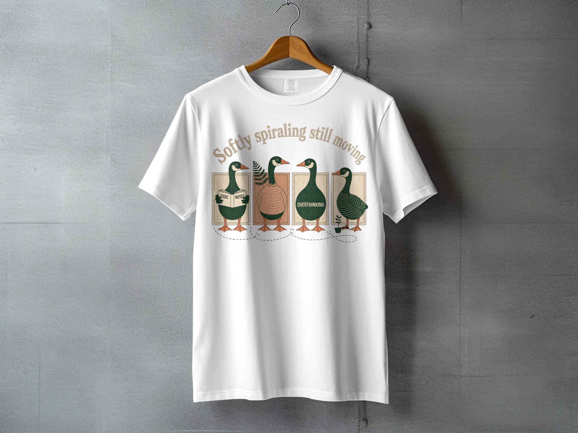 White t-shirt with four ducks reading books and the text "Softly spiraling still moving."