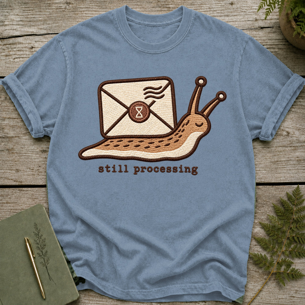 Blue t-shirt with embroidered snail carrying an envelope and the text "still processing".
