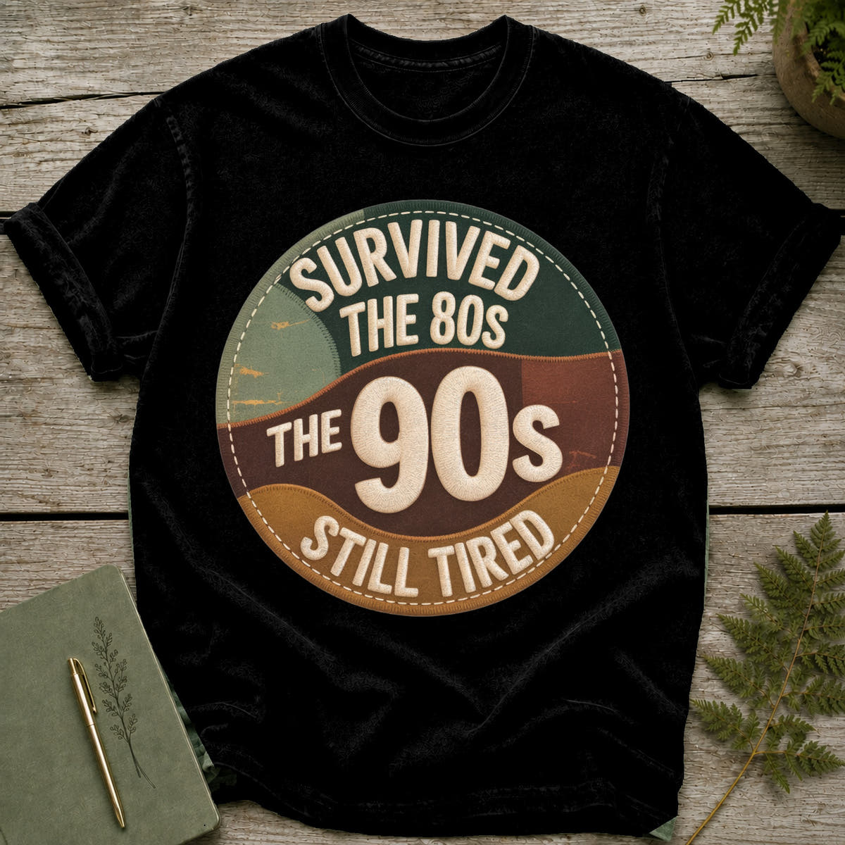 Black t-shirt with "Survived the 80s, The 90s, Still Tired" circular graphic.