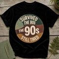 Black t-shirt with "Survived the 80s, The 90s, Still Tired" circular graphic.