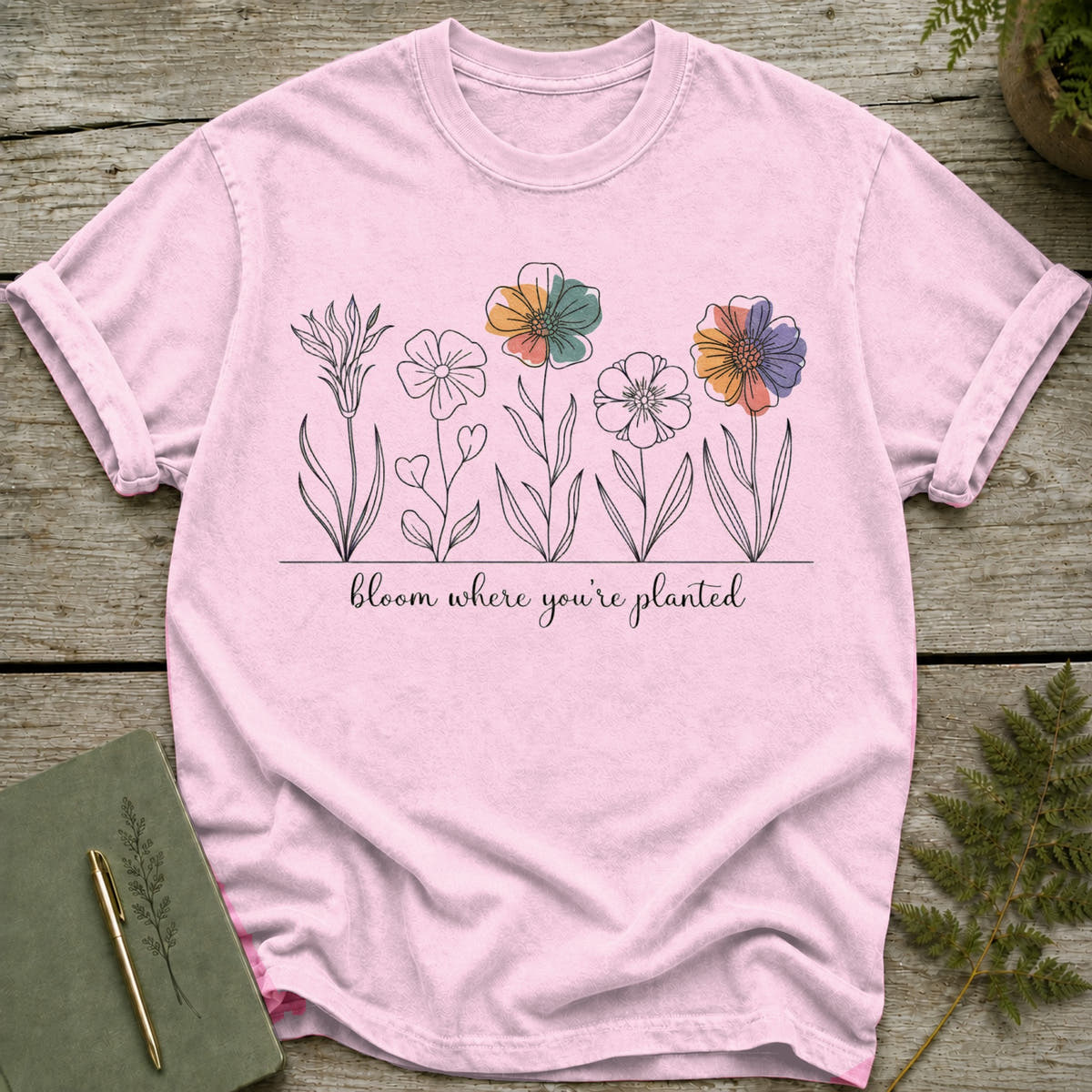 Pink t-shirt with line drawing of flowers and the text "bloom where you're planted".