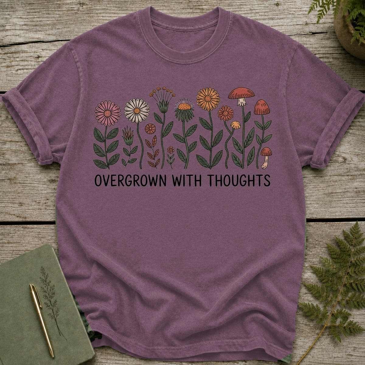 Purple t-shirt with floral and mushroom illustration and text "OVERGROWN WITH THOUGHTS".