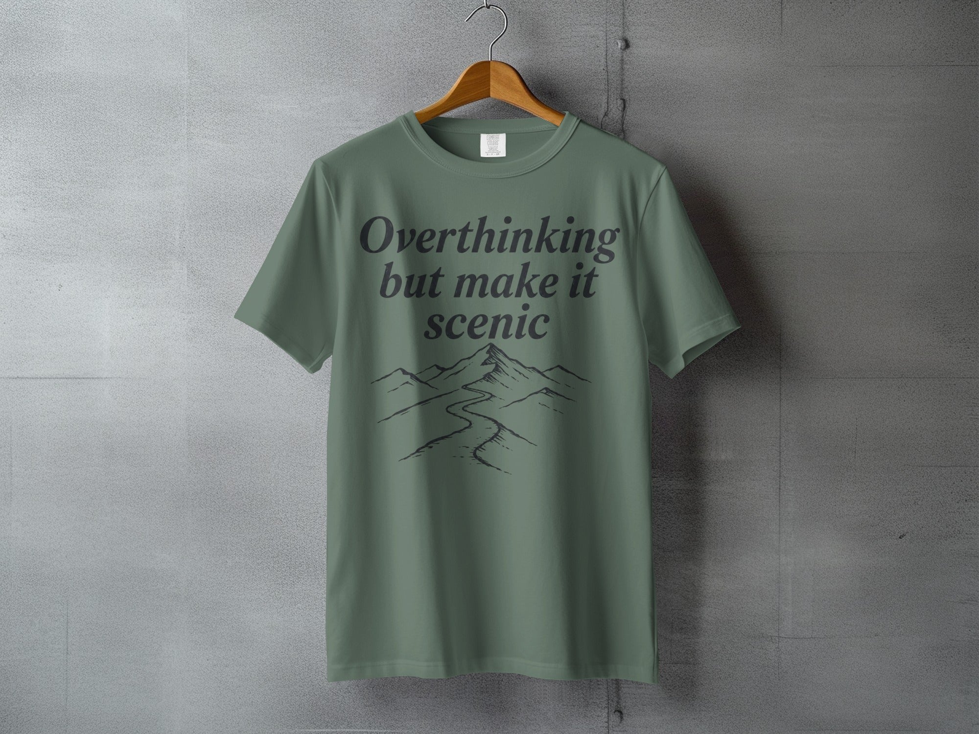 Green t-shirt with "Overthinking but make it scenic" text and mountain outline design.