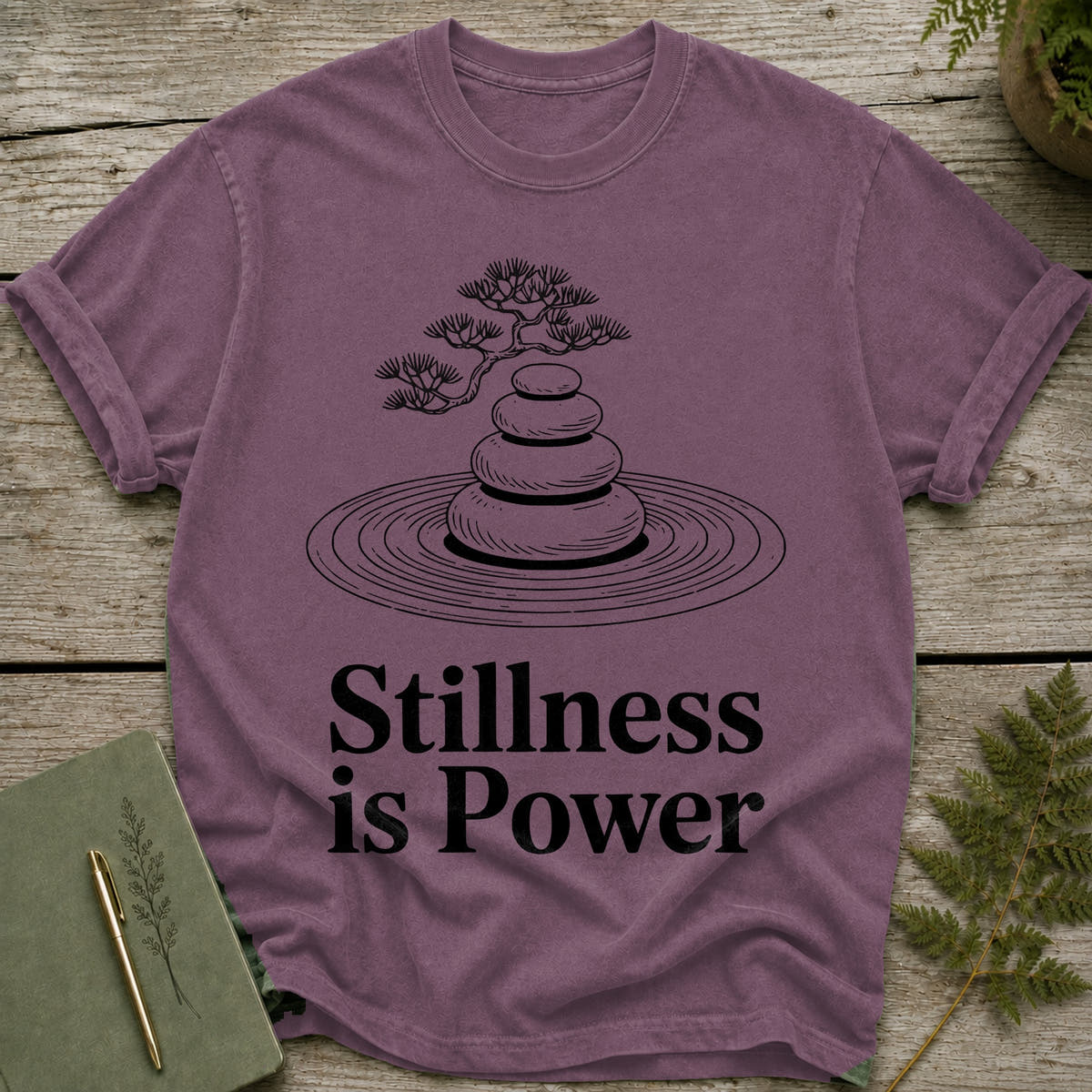 Plum t-shirt with black line art of stacked stones and a bonsai tree with text "Stillness is Power".