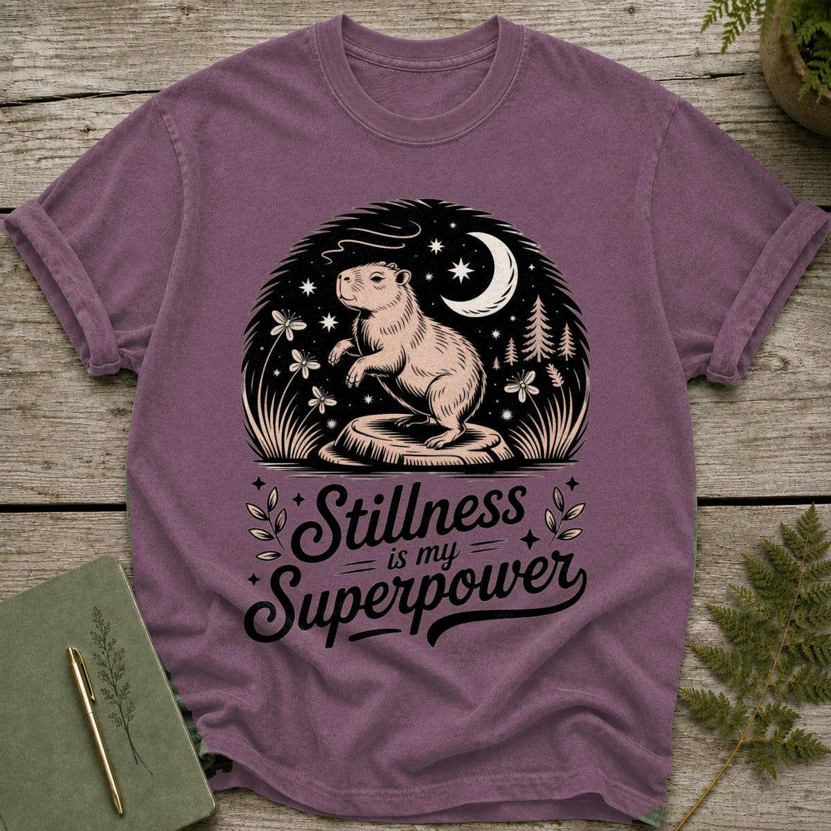 Purple t-shirt with a capybara, moon, stars, and text "Stillness is my Superpower".