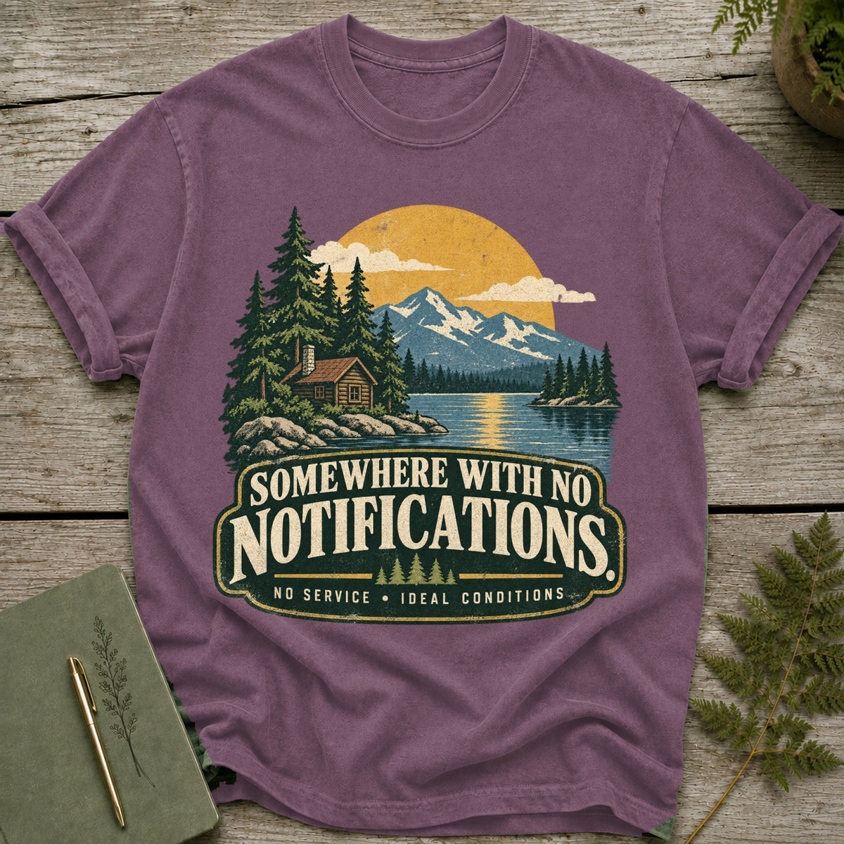 T-shirt graphic with a cabin, lake, mountains, and text "Somewhere with no notifications."