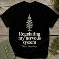 Black t-shirt with a pine tree and text: "Regulating my nervous system, Poorly, but outdoors."