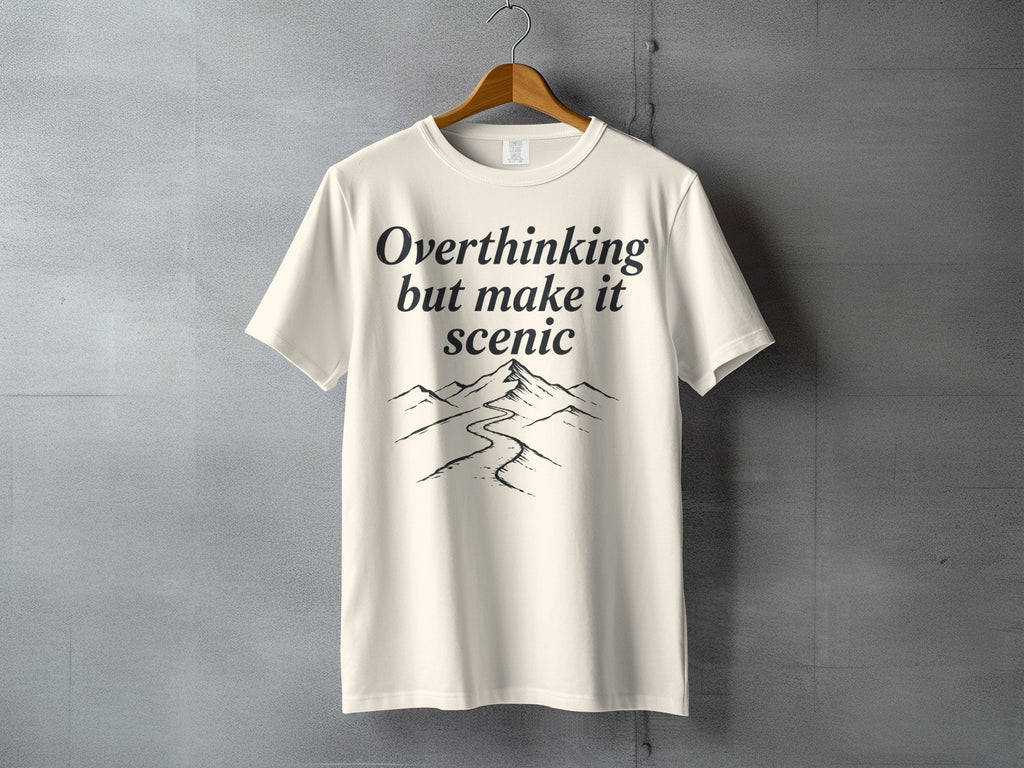 Cream t-shirt with "Overthinking but make it scenic" text and mountain landscape graphic.