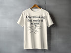 Cream t-shirt with "Overthinking but make it scenic" text and mountain landscape graphic.
