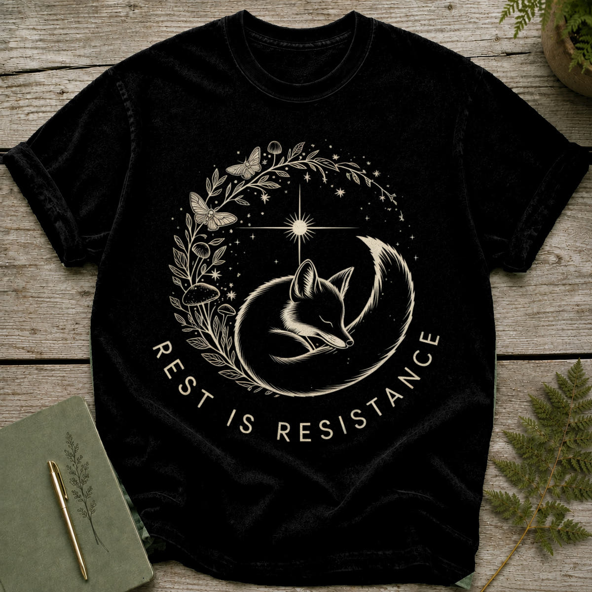 Black t-shirt with a circular design of a sleeping fox, mushrooms, butterflies, and stars.