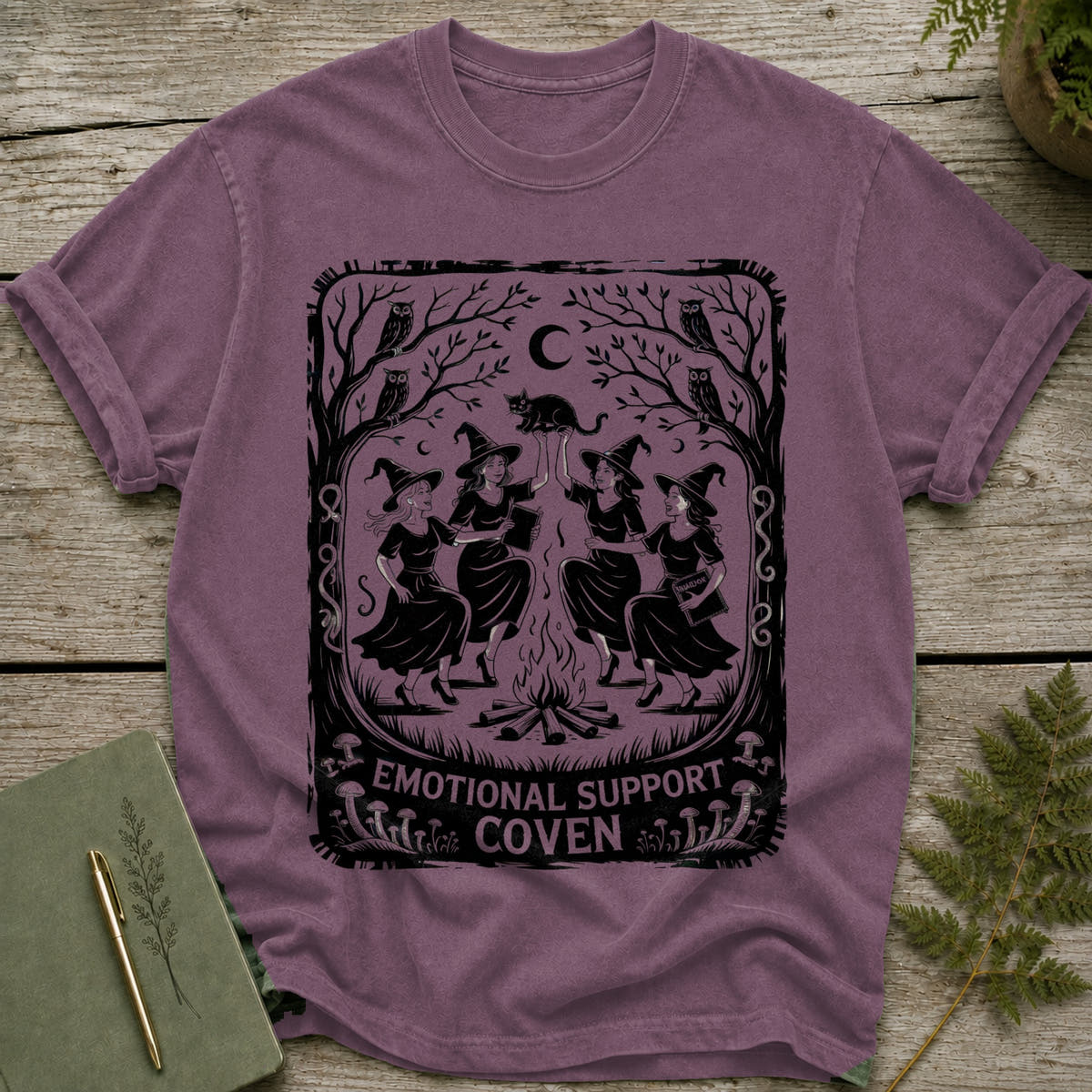 T-shirt with witches dancing around a fire with a black cat overhead.