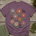 Purple t-shirt with smiling cartoon flowers and text "Bloom Wildly," "Spread Joy," "Find Your Sunshine."