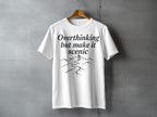White t-shirt with black text "Overthinking but make it scenic" and mountain graphic.