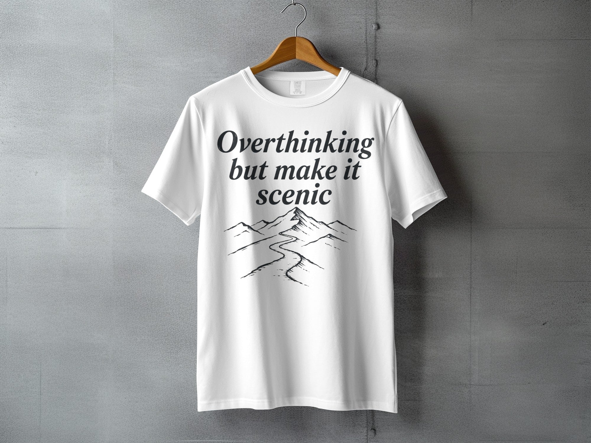 White t-shirt with black text "Overthinking but make it scenic" and mountain graphic.