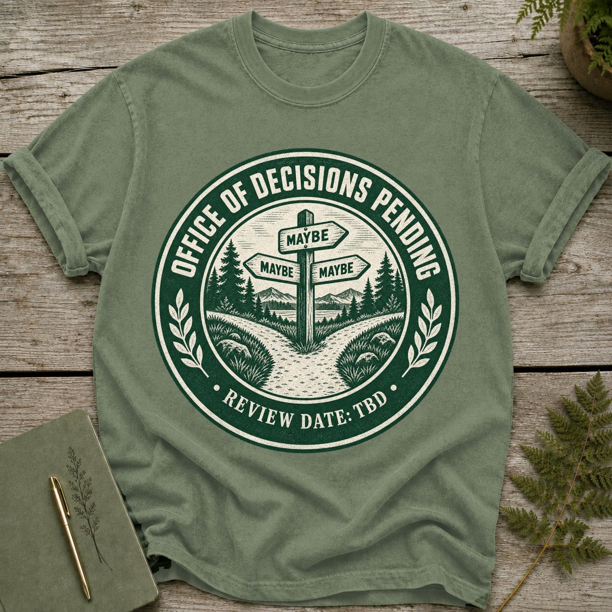 Green t-shirt with circular design featuring a signpost with "MAYBE" directions.