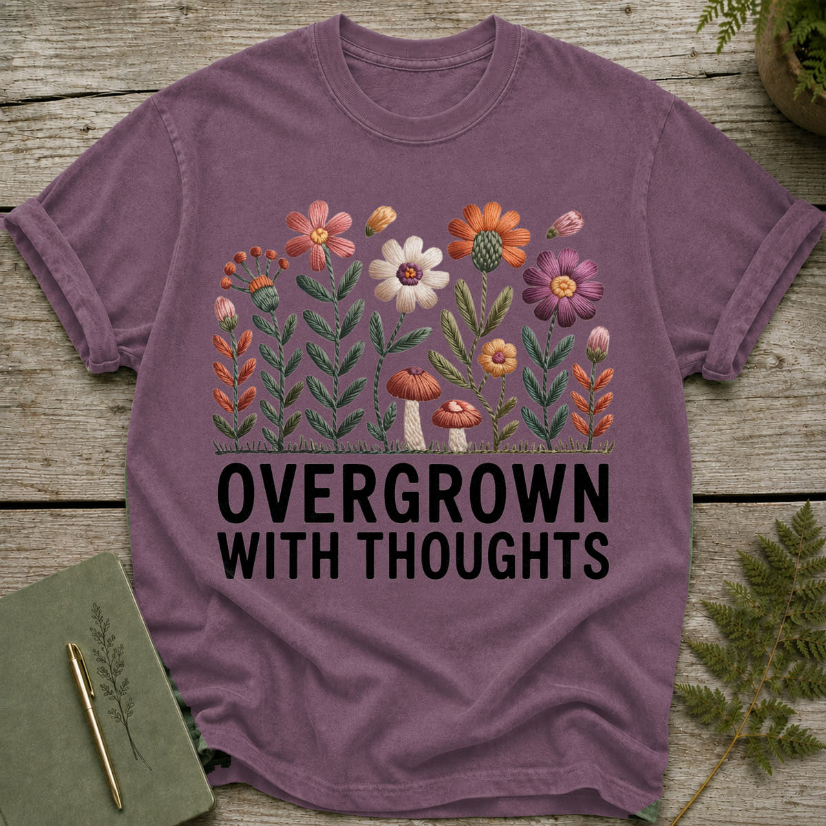 Purple t-shirt with embroidered flowers and text "OVERGROWN WITH THOUGHTS".